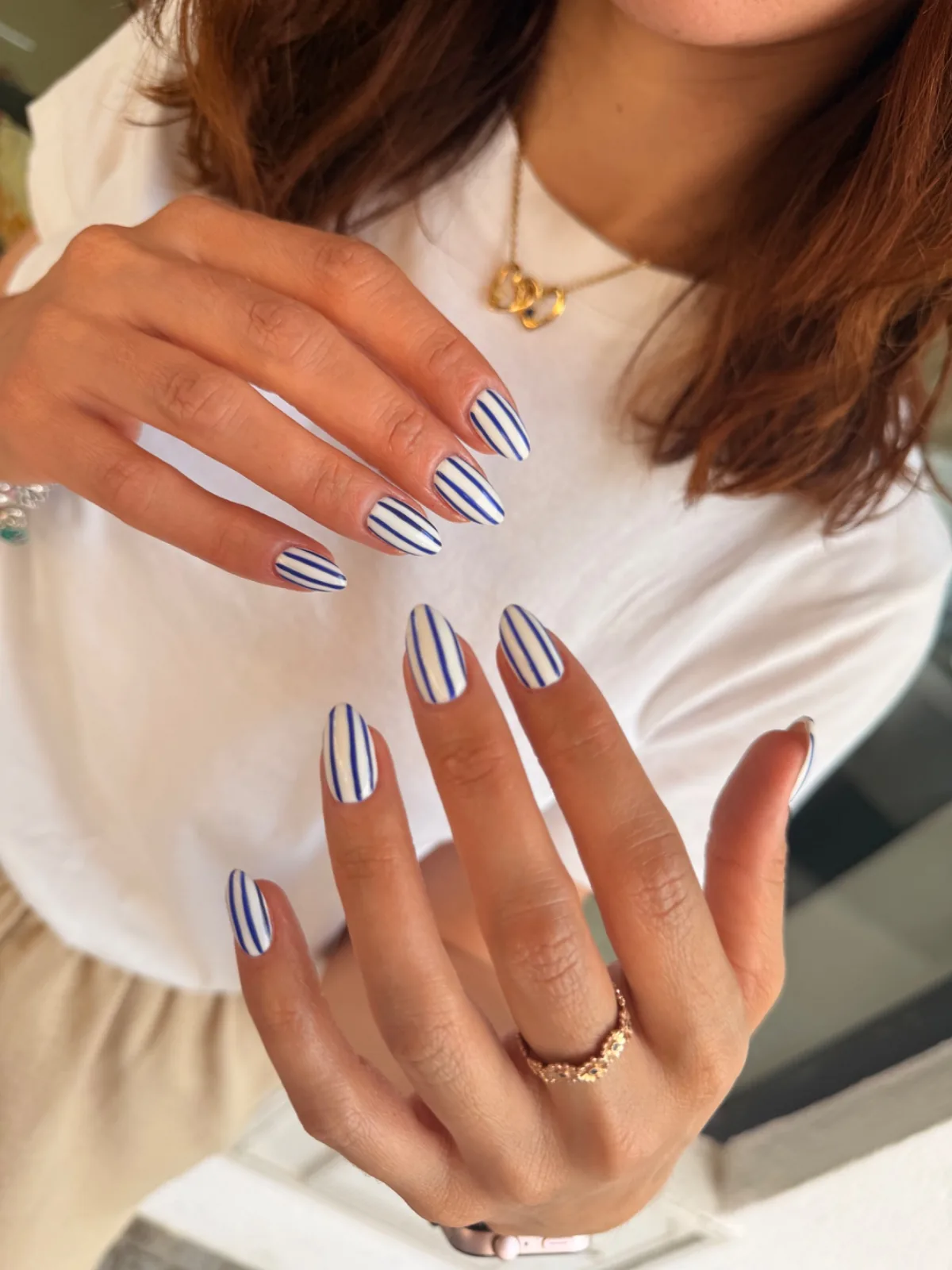 Uñas almendradas blancas con rayas azules marino, mostradas con ambas manos